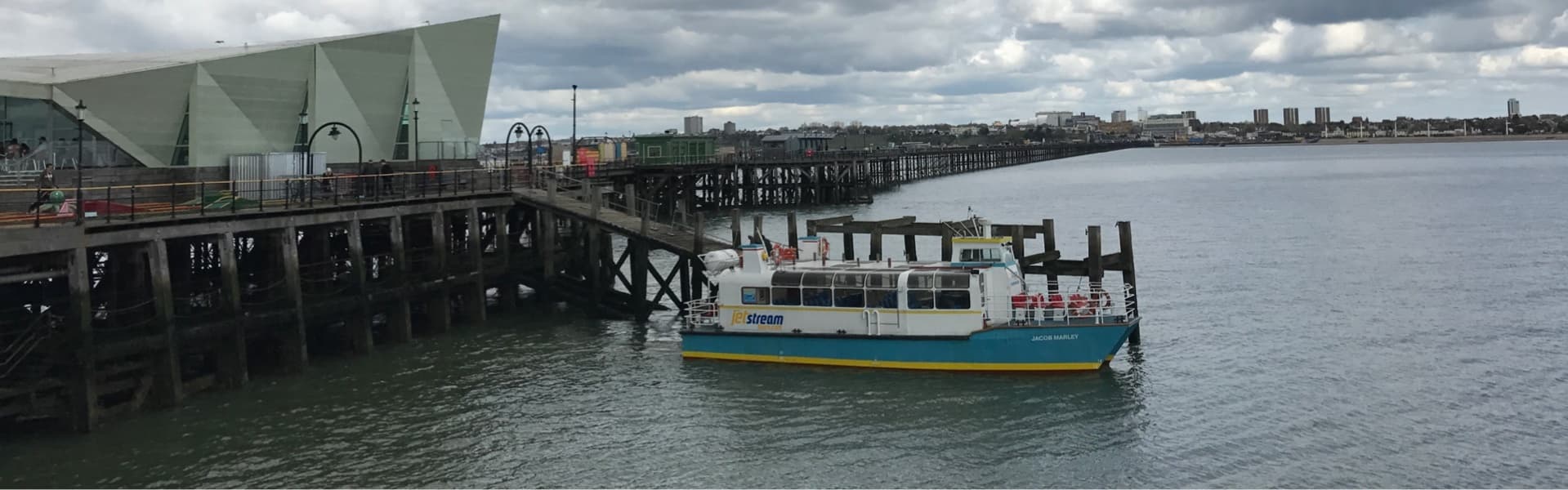 Coastal passenger ferry approaching seaside pier under clouds