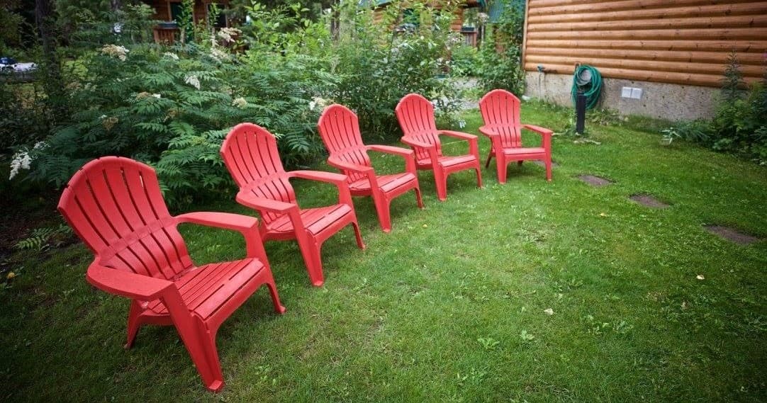 Row of red Adirondack chairs on grassy lawn by rustic cabin