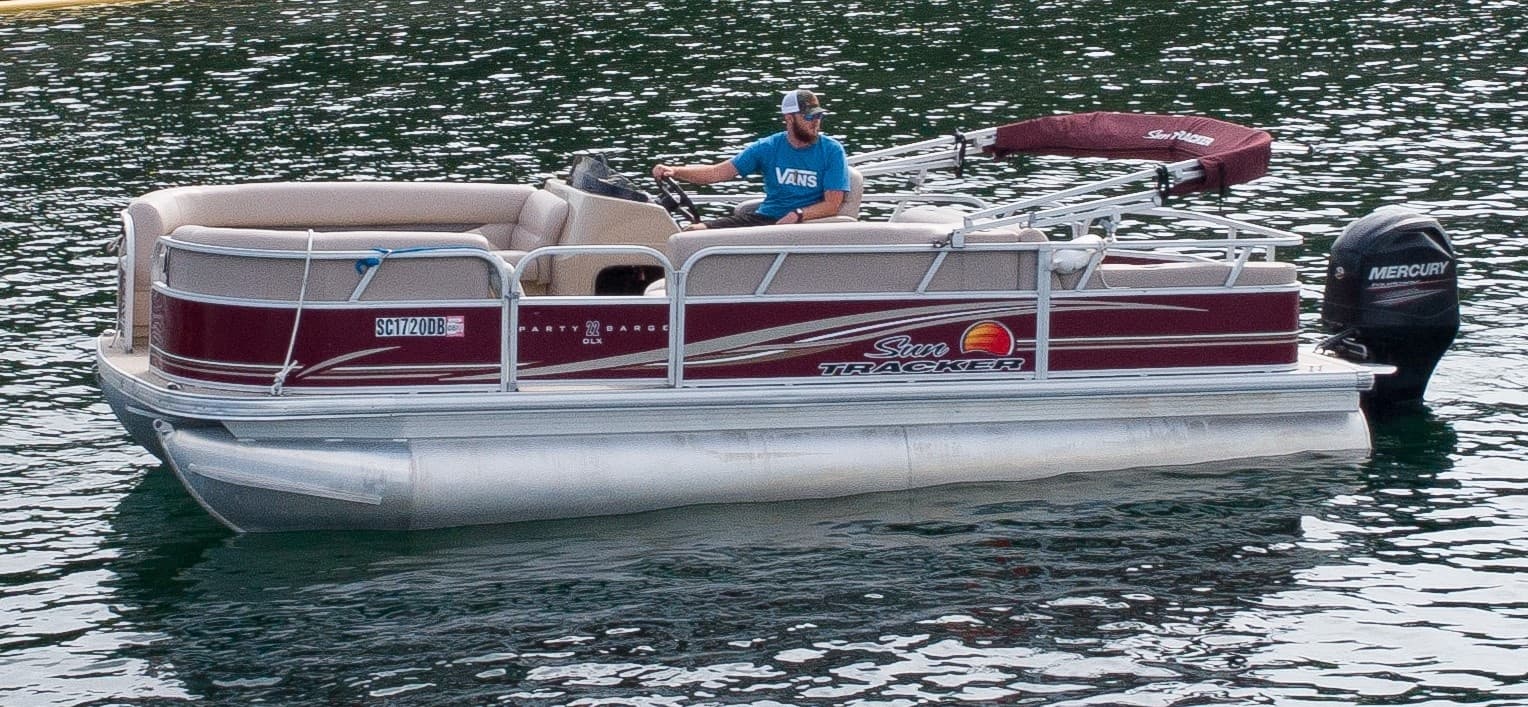 Maroon pontoon boat on sparkling lake with wooded shoreline
