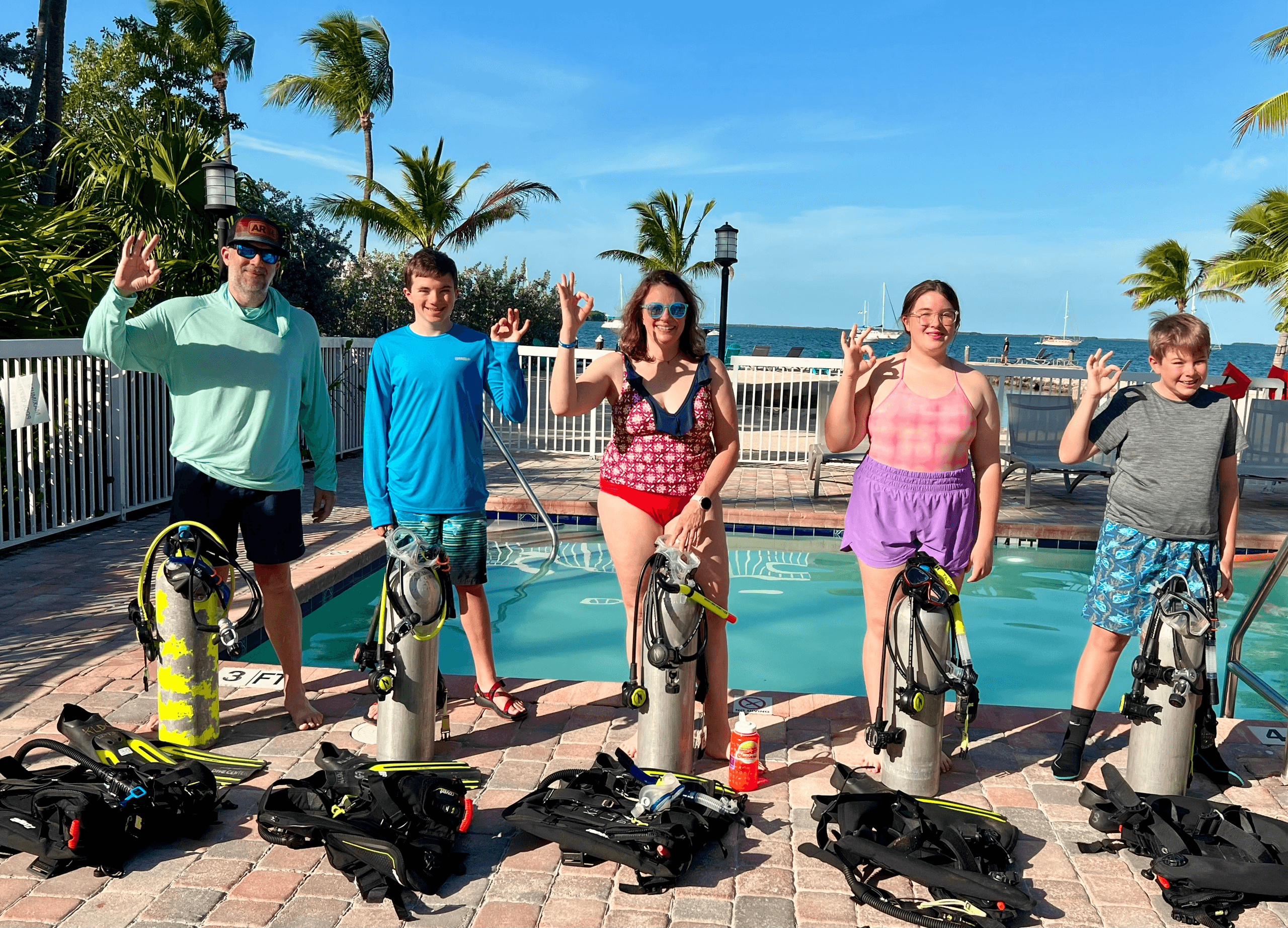 Divers posing with gear on sunny dock by palm trees