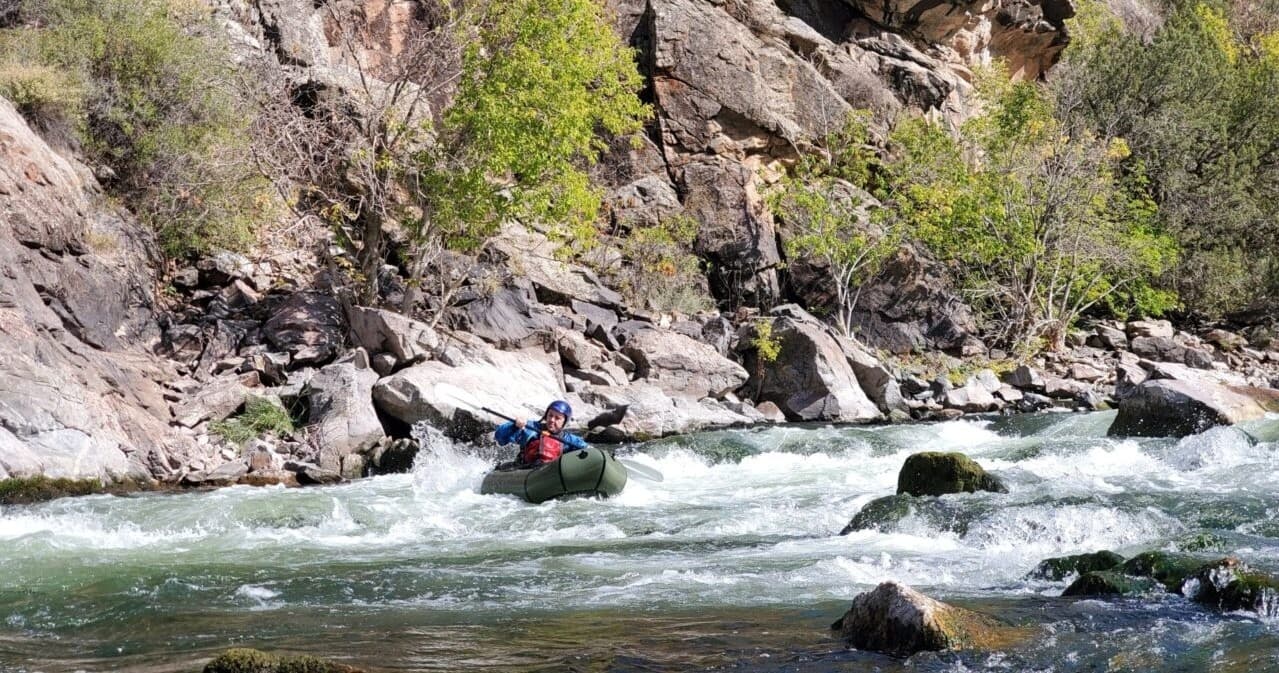 Packrafter running technical rapids through rocky canyon river