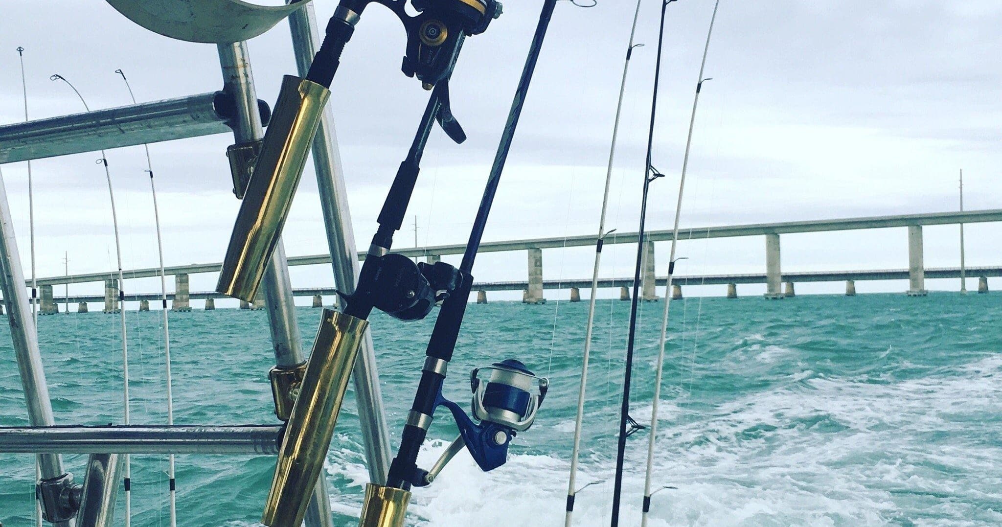 Fishing rods and tackle on boat over turquoise sea near bridge