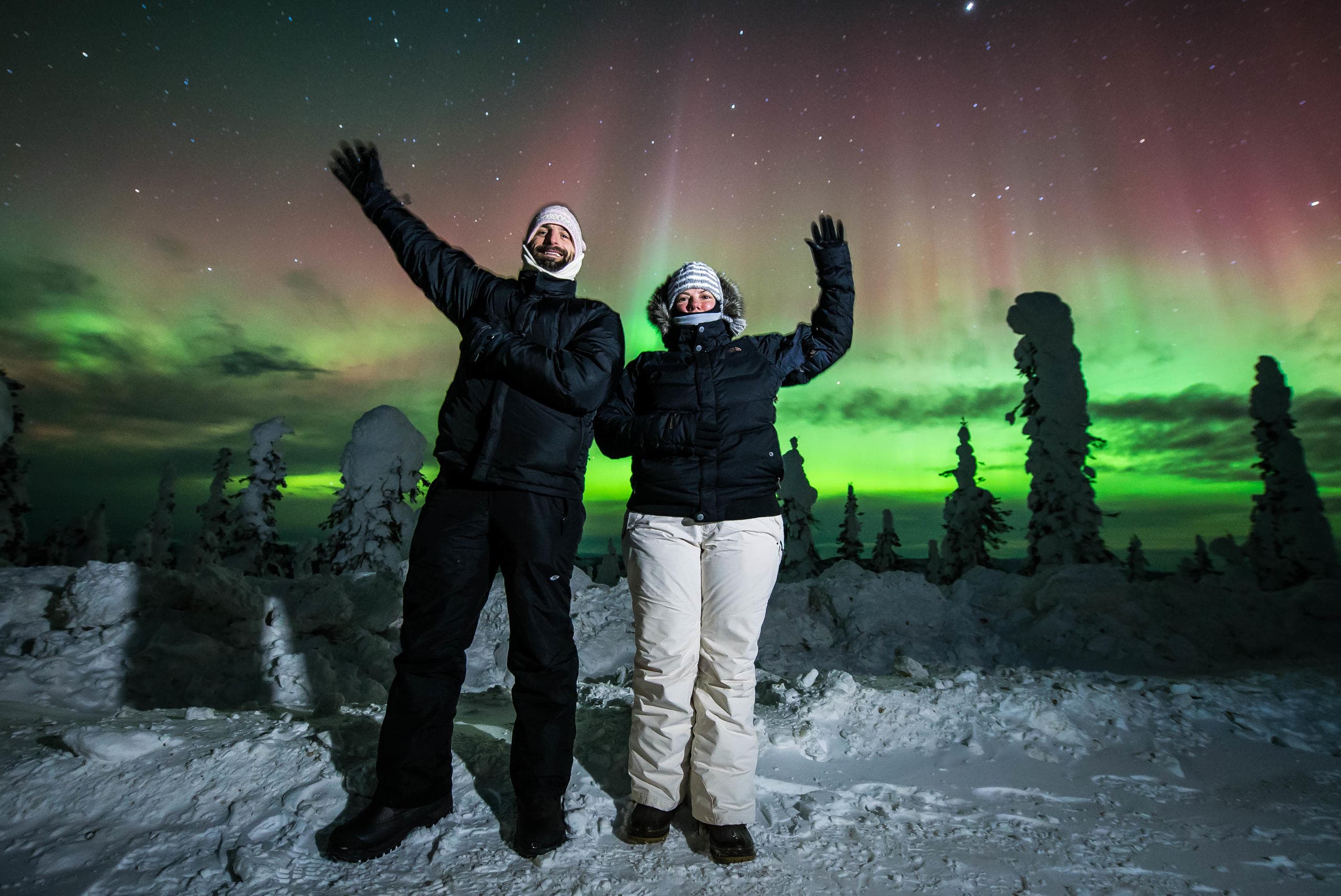Tourists cheering under aurora borealis in snowy nighttime field