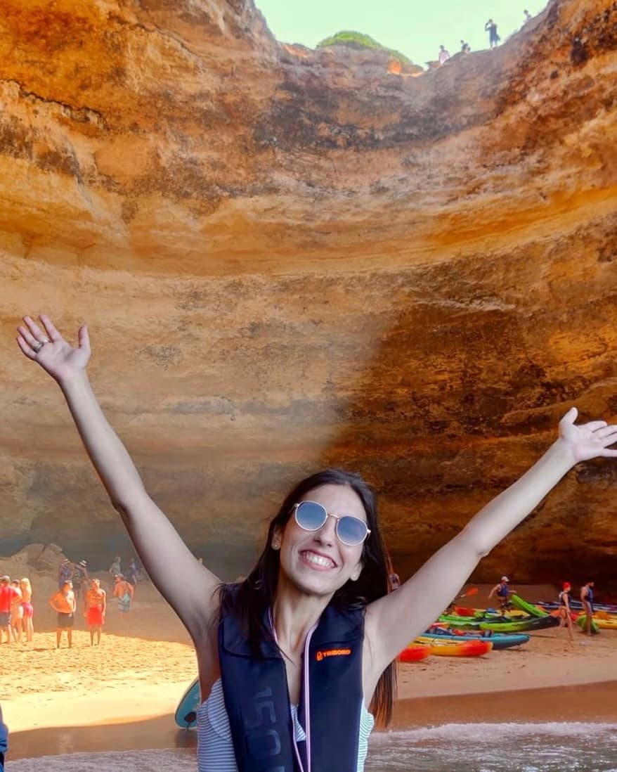 Smiling woman posing inside dramatic coastal sea cave with kayaks
