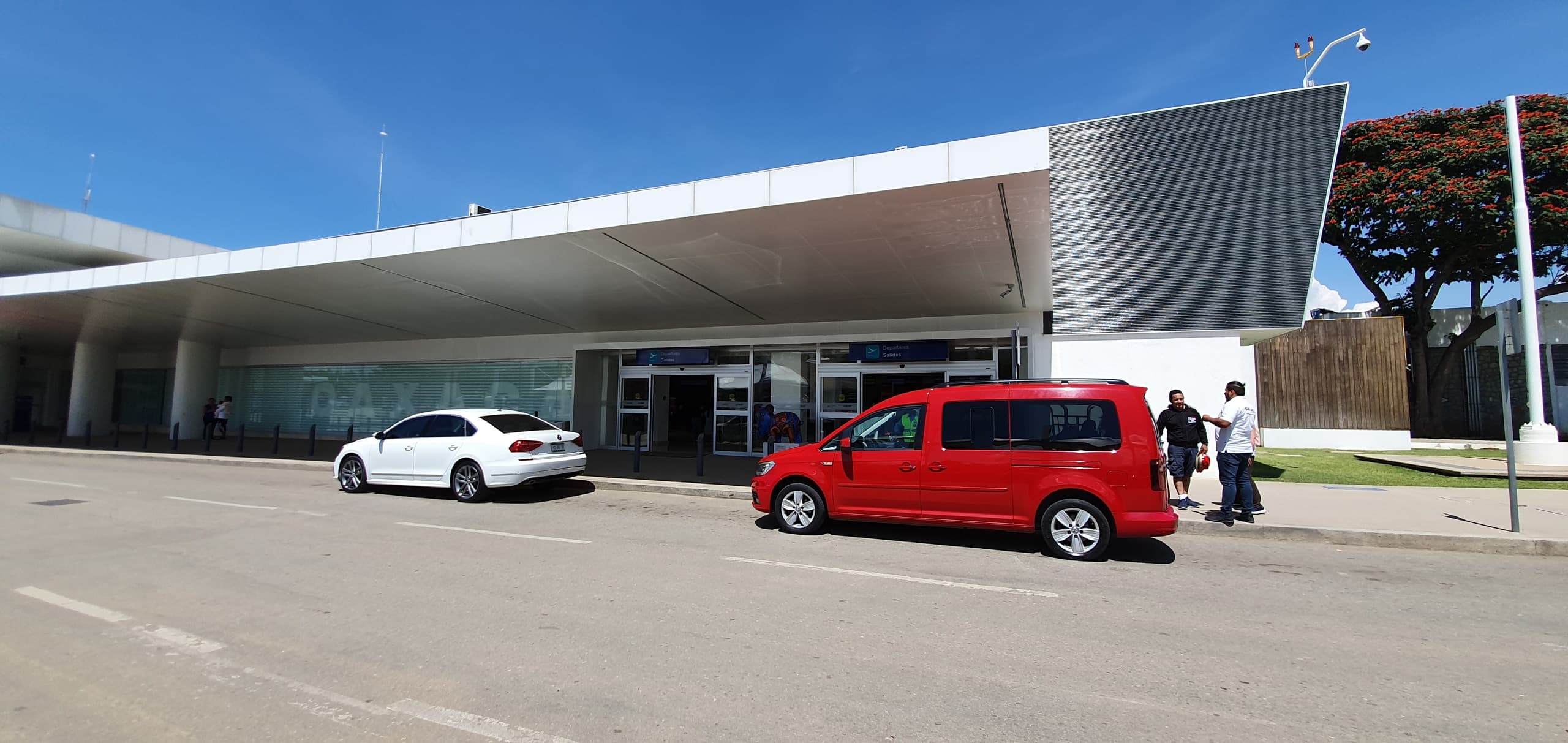 Passengers outside airport terminal with shuttle vehicles parked