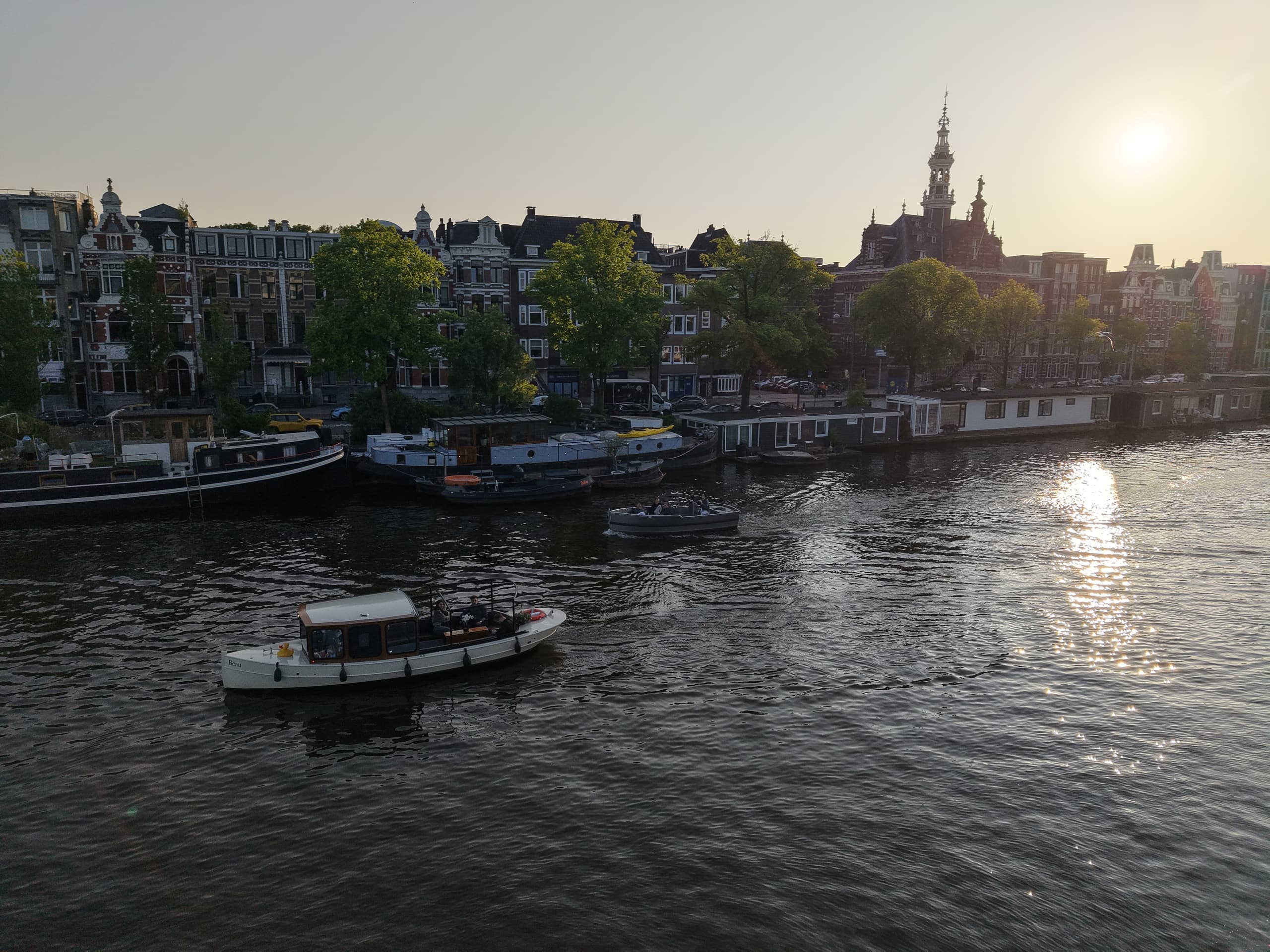 Tour boat cruising Amsterdam canal at sunset with city skyline