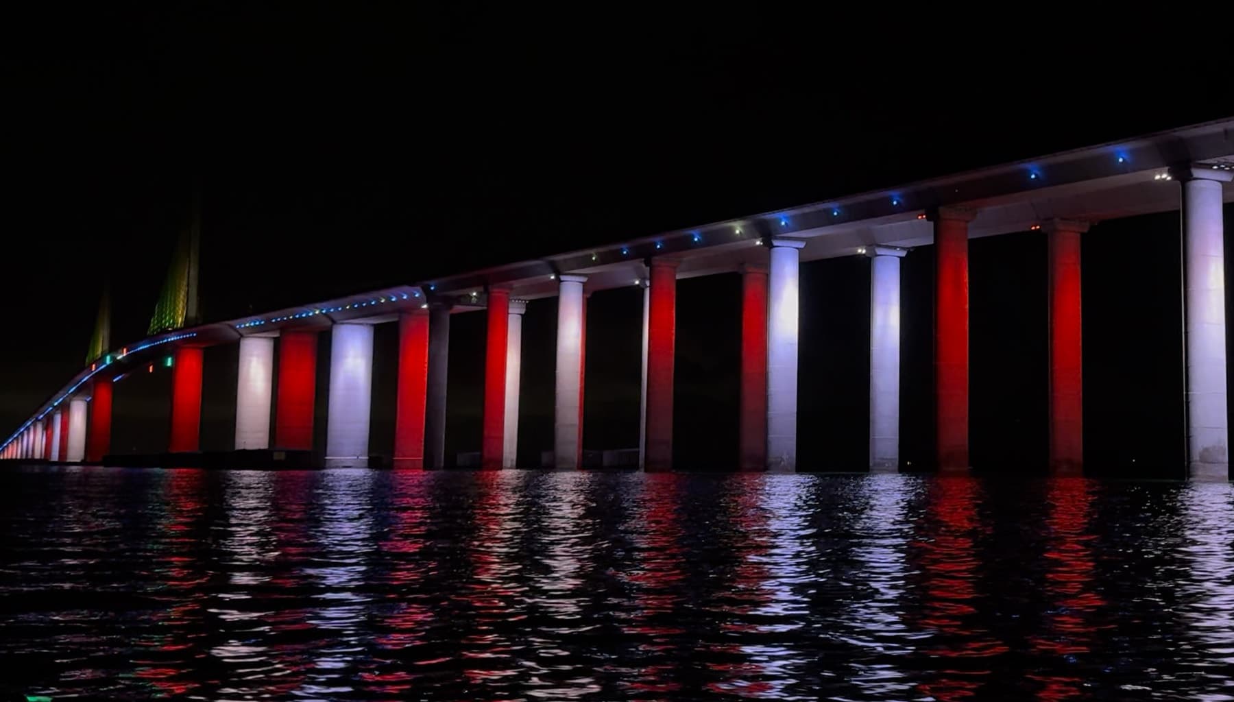 Illuminated waterfront bridge at night reflecting red lights