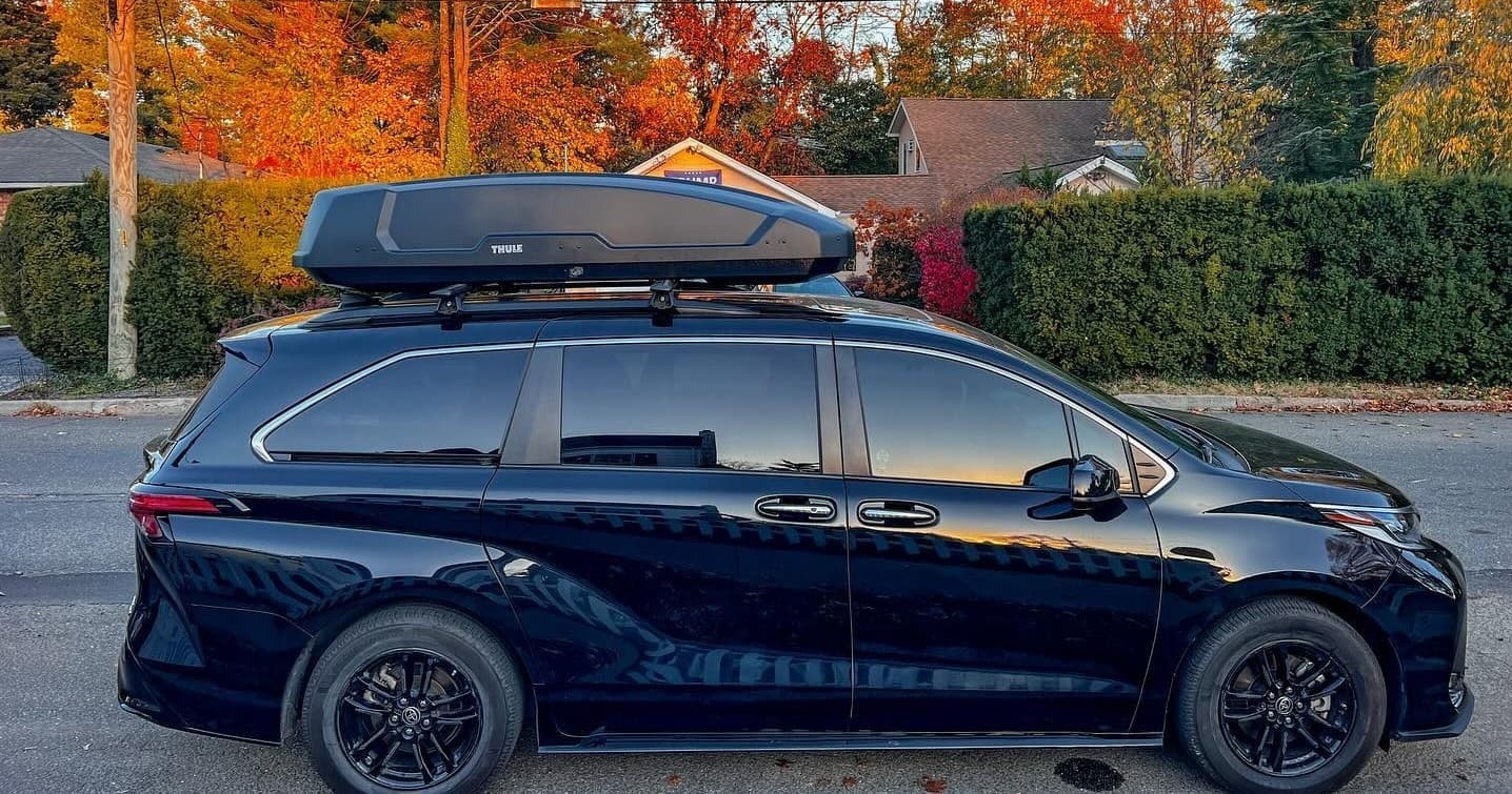 Black minivan with rooftop cargo box by autumn neighborhood road