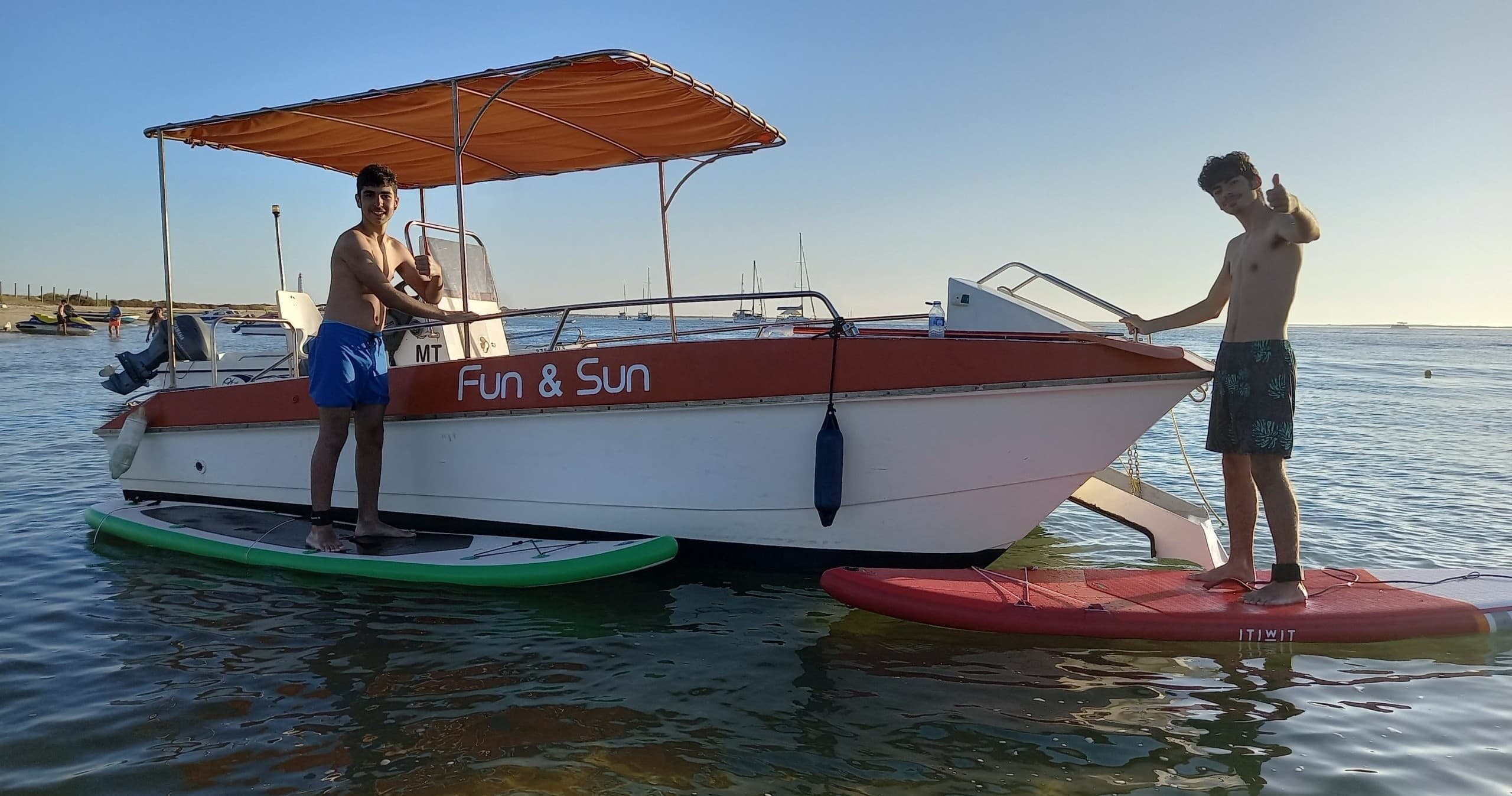 Two people paddleboarding beside a small tour boat on sea