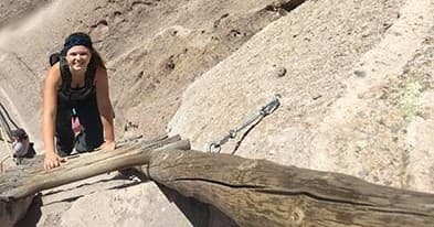 Woman scrambling rock via ladder on steep canyon cliff