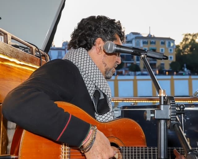 Guitarist performing on riverboat deck with city buildings backdrop
