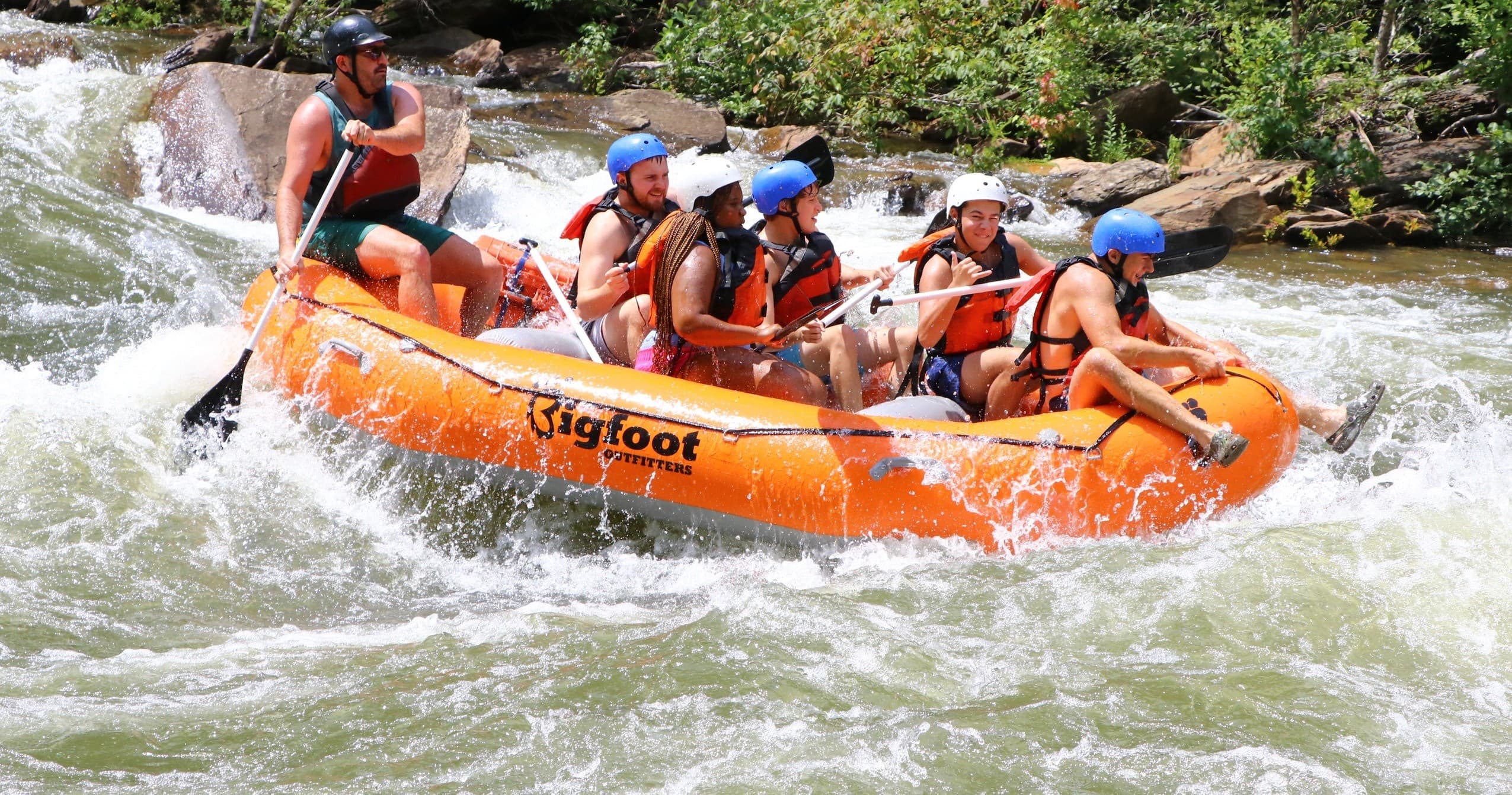 Large rafting crew charging down steep river rapids in canyon