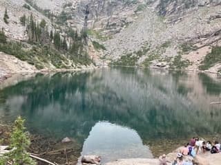 Crystal alpine lake with hikers on shore, high mountain hiking lake