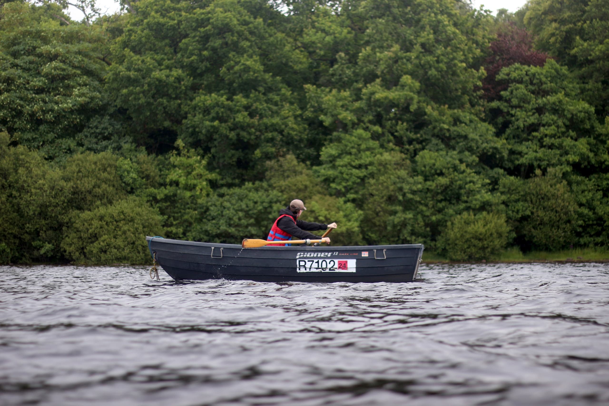 Single angler in small boat on Loch Lomond surrounded by trees