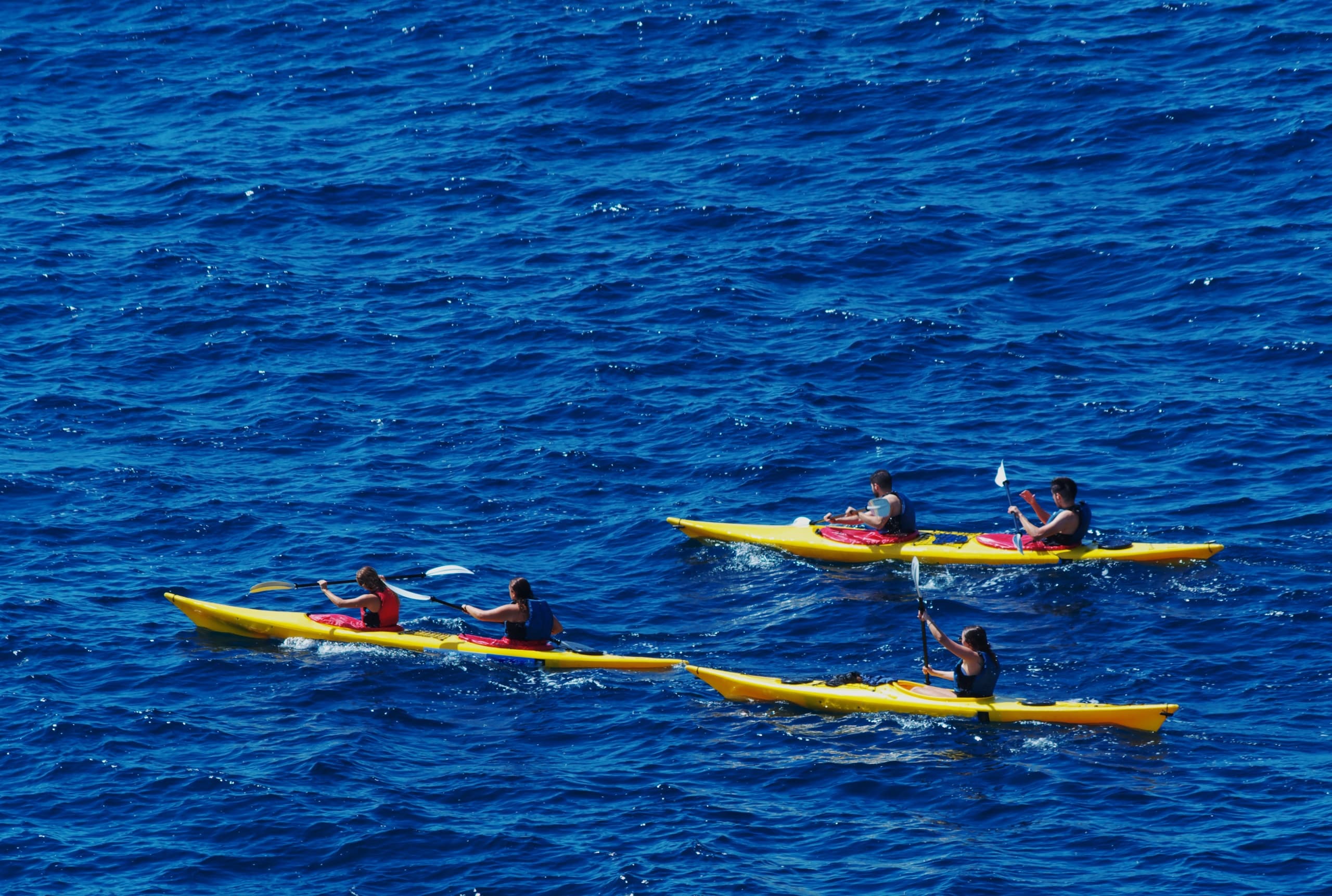 Two kayakers paddling across deep blue open ocean