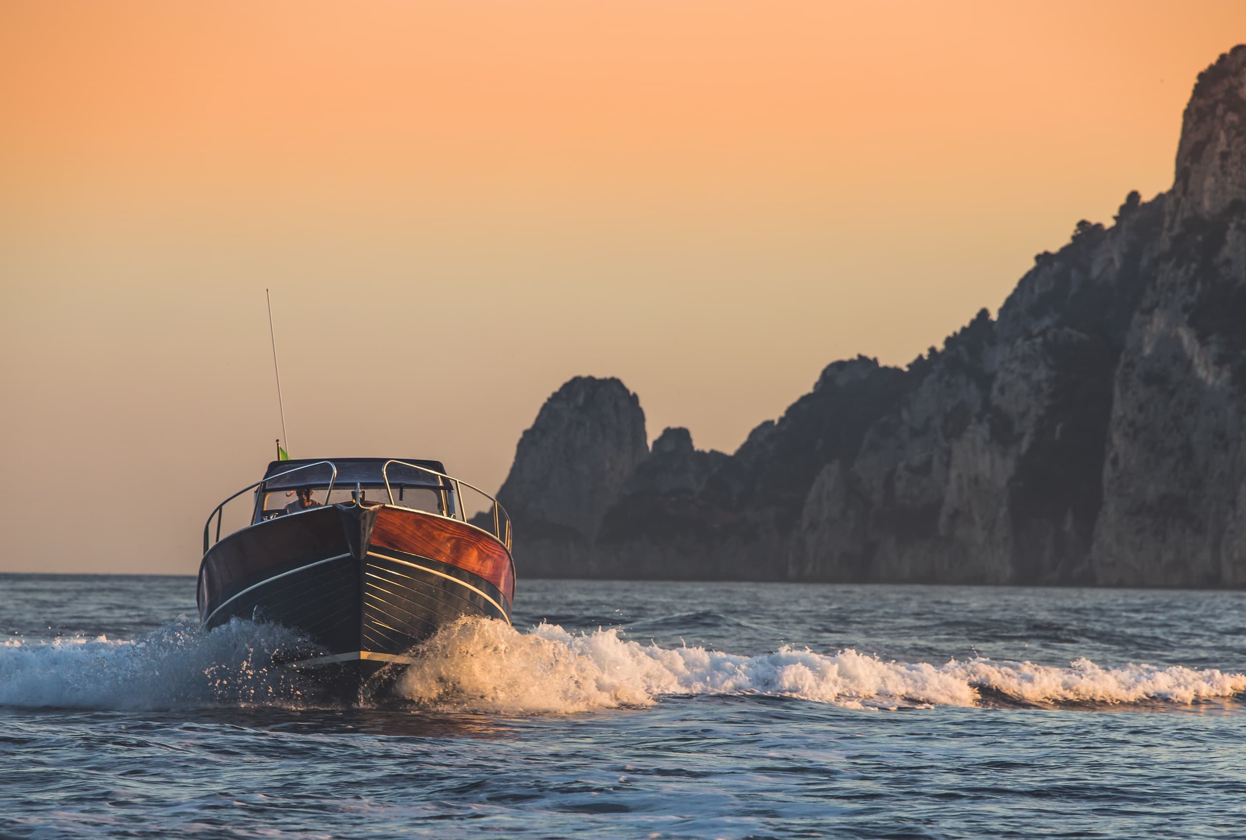 Motorboat speeding at sunset past rocky coastal cliffs