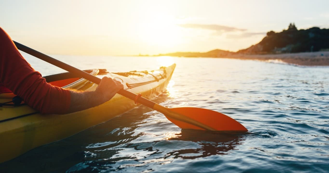 Solo kayaker paddling at sunset on coastal open water