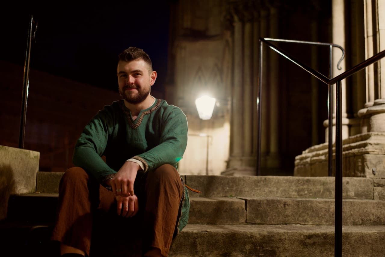 Guide seated on stone steps outside historic York cathedral at night