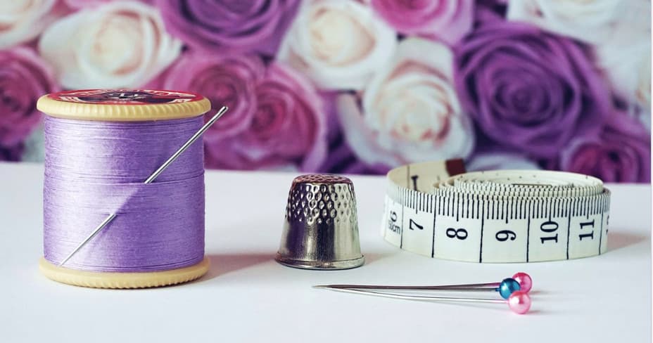 Purple thread, thimble and tape measure on floral table