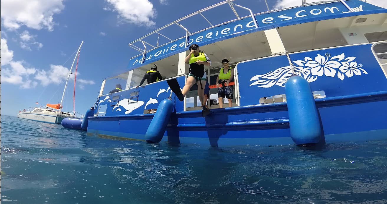 Snorkel boat and guests boarding from blue vessel on ocean off Hawaii