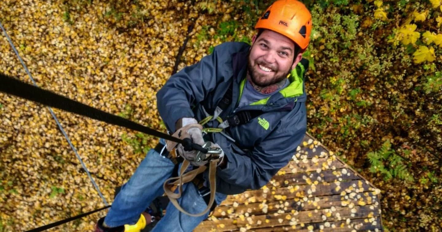 Man ziplining above autumn forest canopy, smiling, action