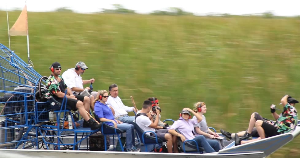 Group on high-speed airboat gliding past marsh vegetation