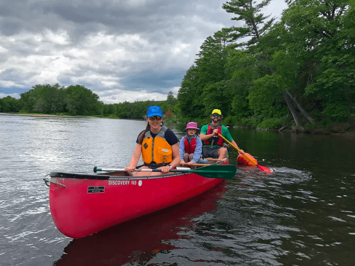 Family canoe trip in a red canoe on a forested calm river