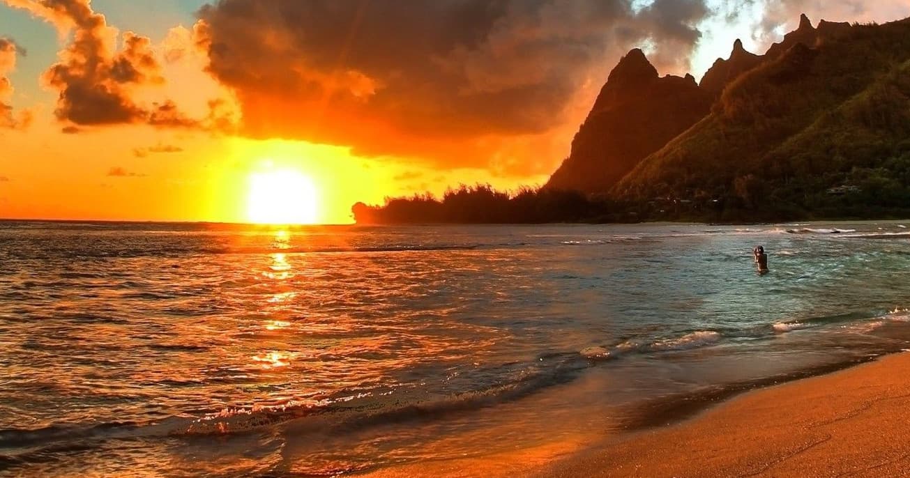 Sunset beach with surfers and volcanic cliffs in Kauai