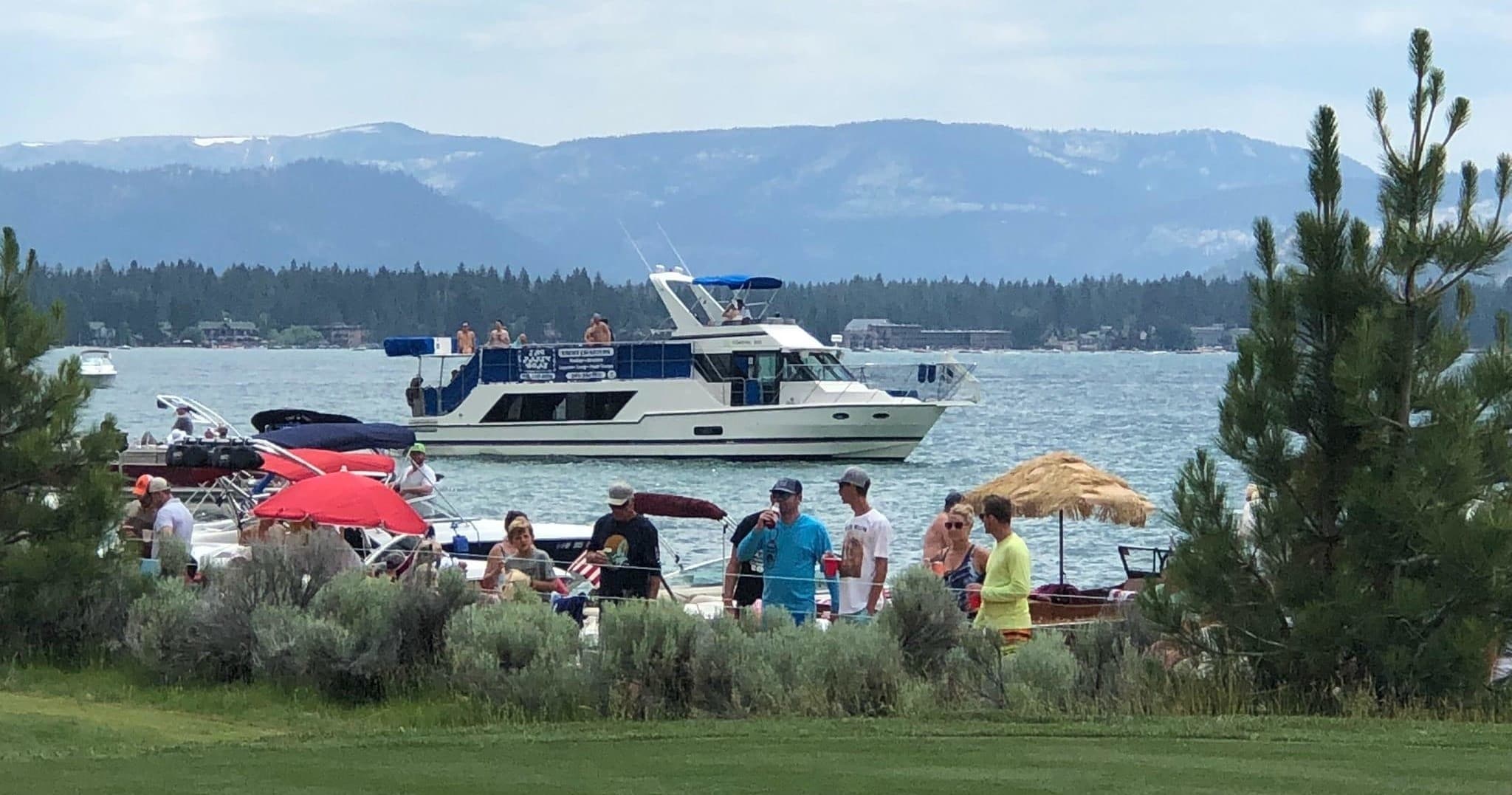 Boats and beachgoers gathered along lakeshore with distant hills
