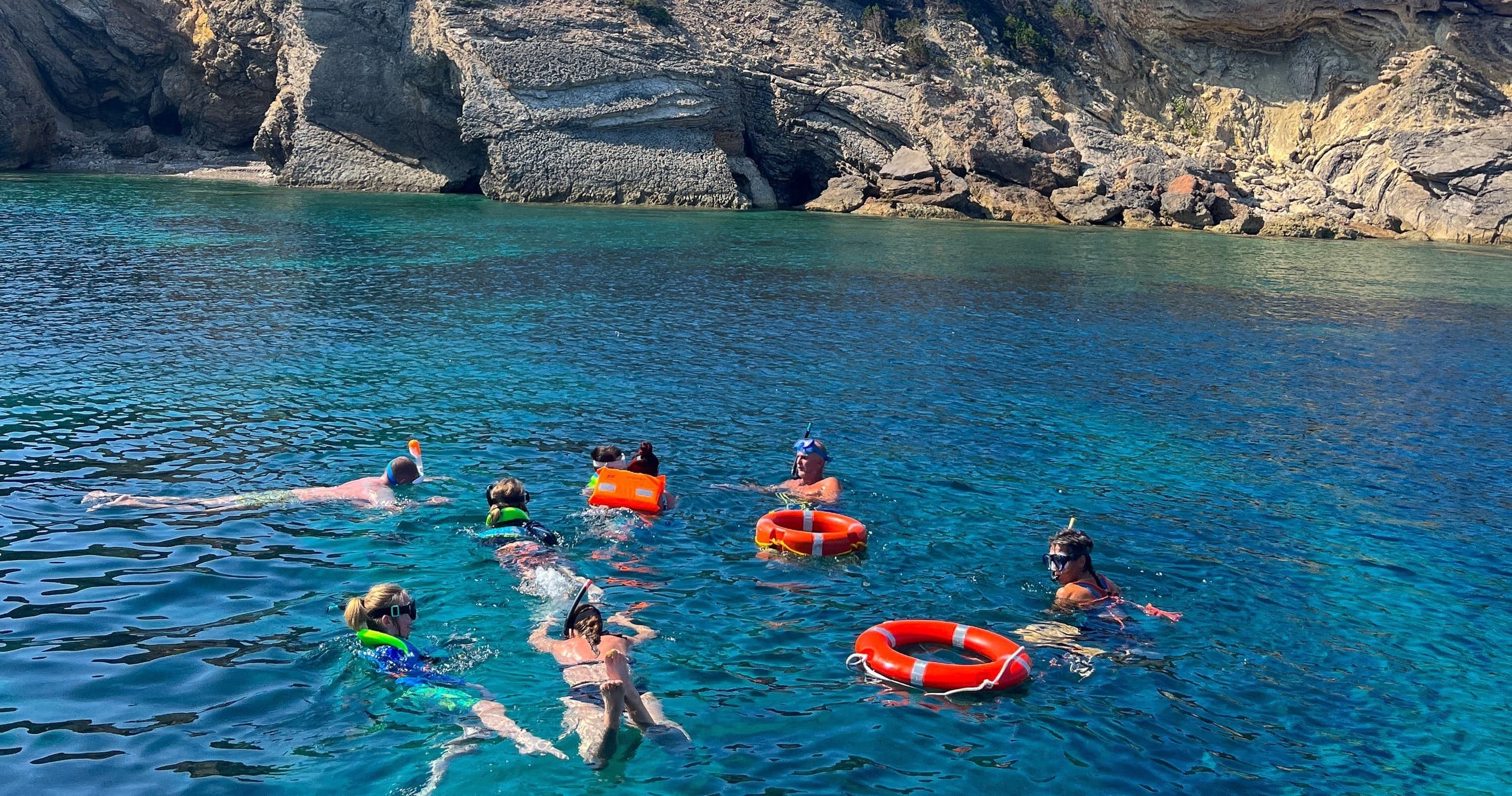 Group snorkeling with safety rings in clear sea by limestone cliffs