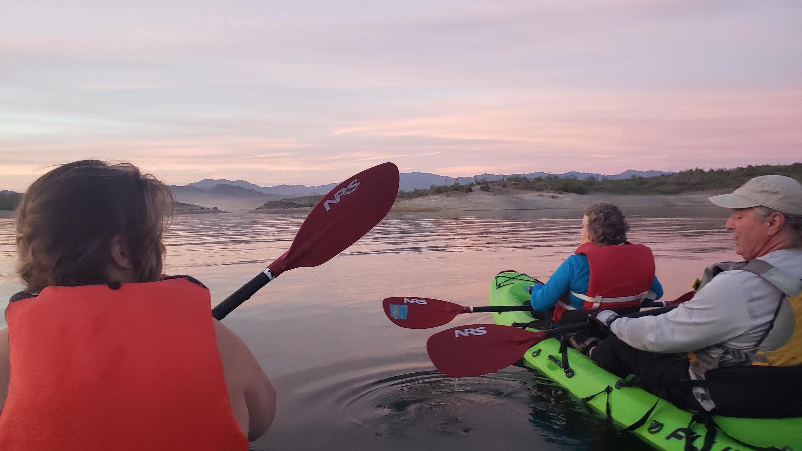 Group kayaking at sunset across a wide reflective river landscape