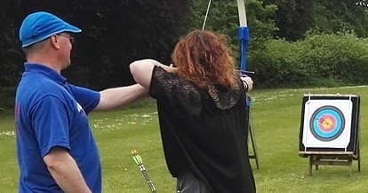 Instructor coaching archer at outdoor target range on lawn