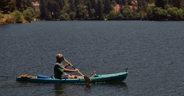 Solo kayaker paddling across calm mountain lake at sunset