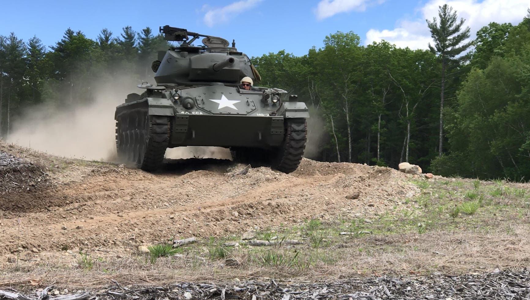 Armored WWII tank cresting a dirt berm in wooded terrain