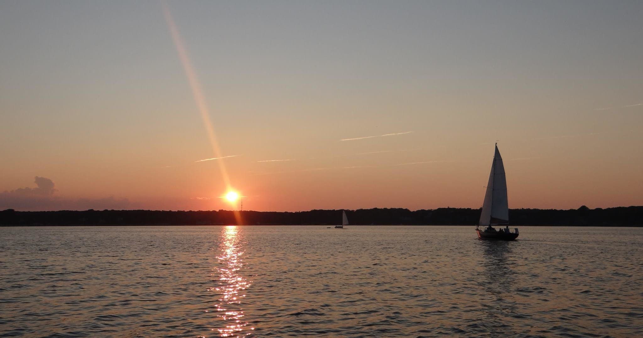 Sailboat silhouetted at sunset over calm ocean waters