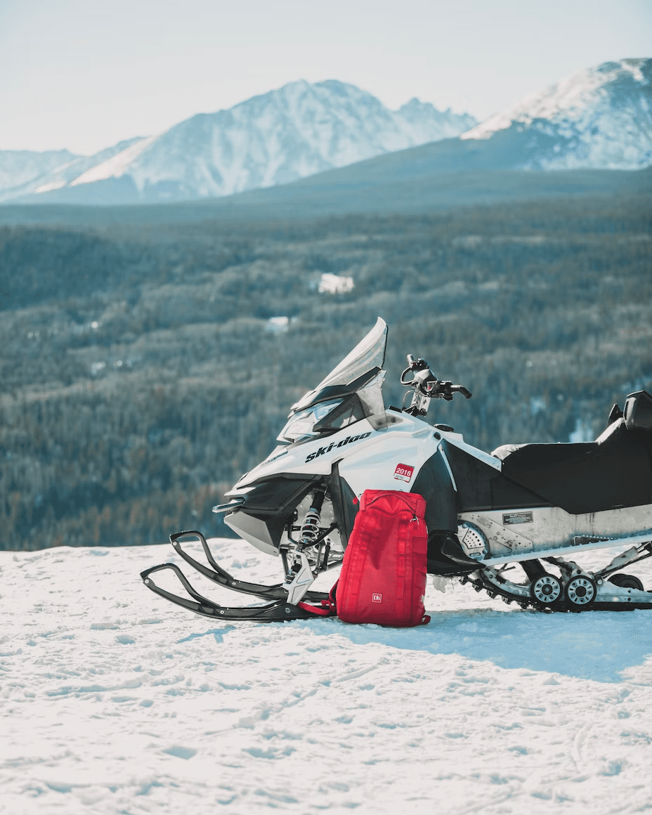 Parked snowmobile on snowy ridge with mountain vista, gear