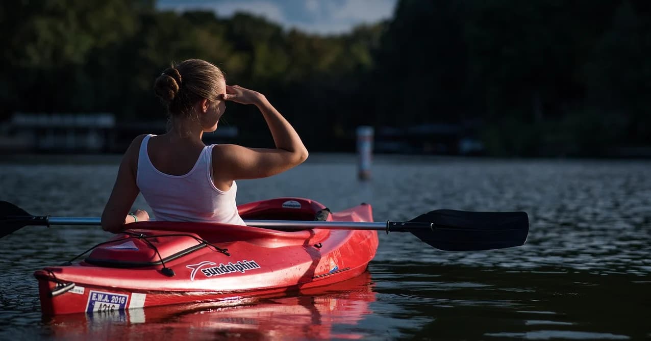 Kayak bow cutting through calm water toward sunrise on open lake