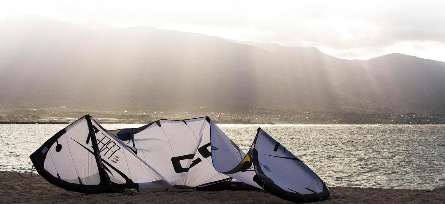 Kite gear on sandy beach with rays breaking over mountains