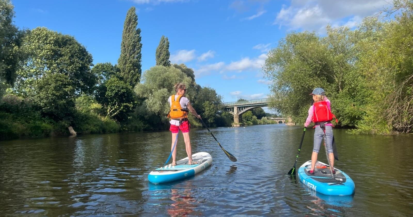 Two paddleboarders touring calm river with bridge in background