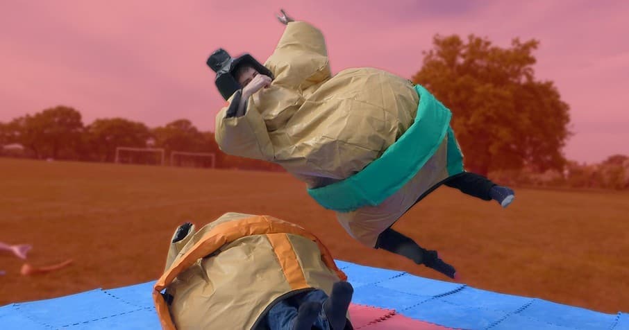 Participants in inflatable sumo suits tumbling on outdoor field