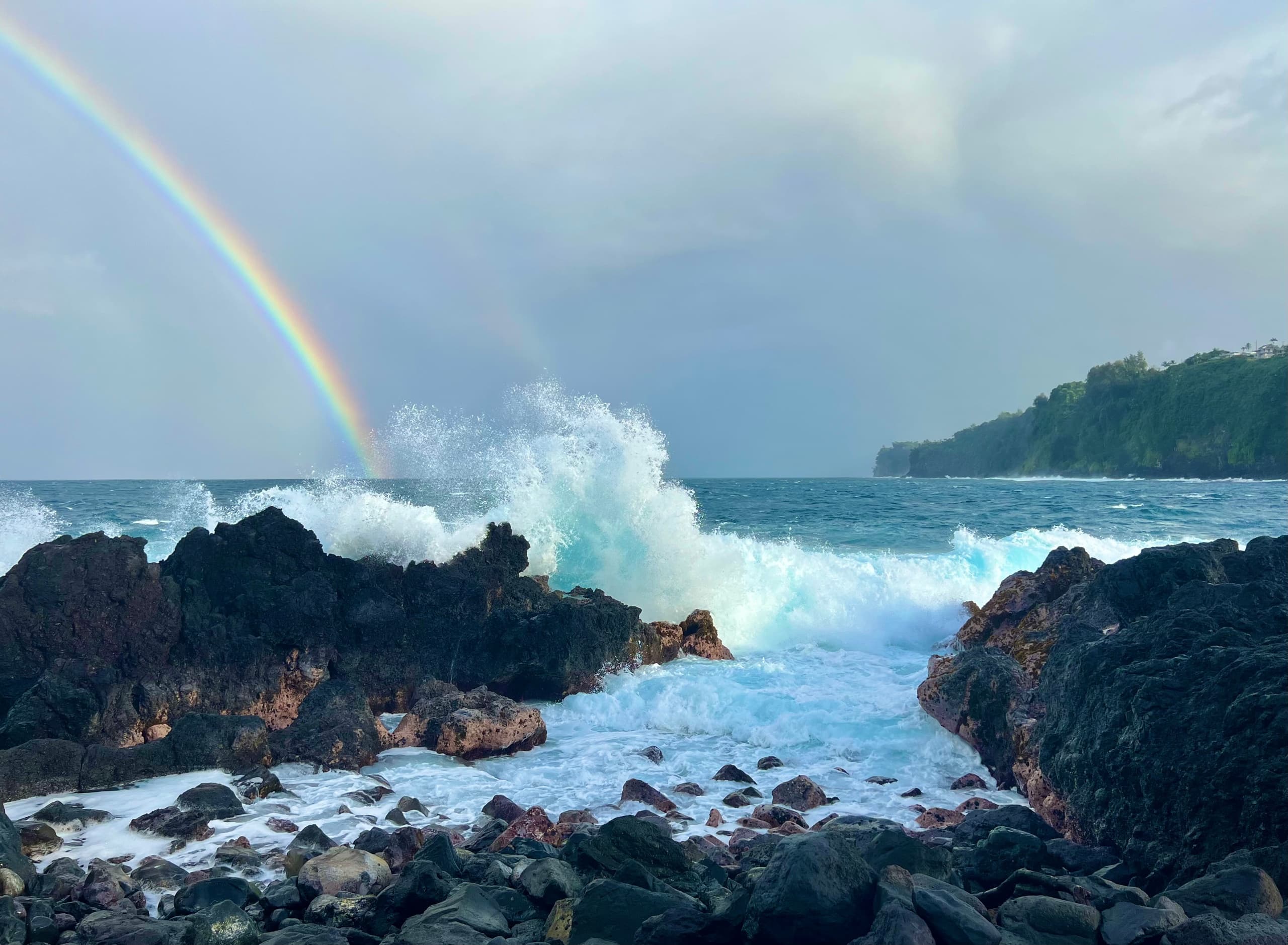 Waves crashing on rocky shore with double rainbow