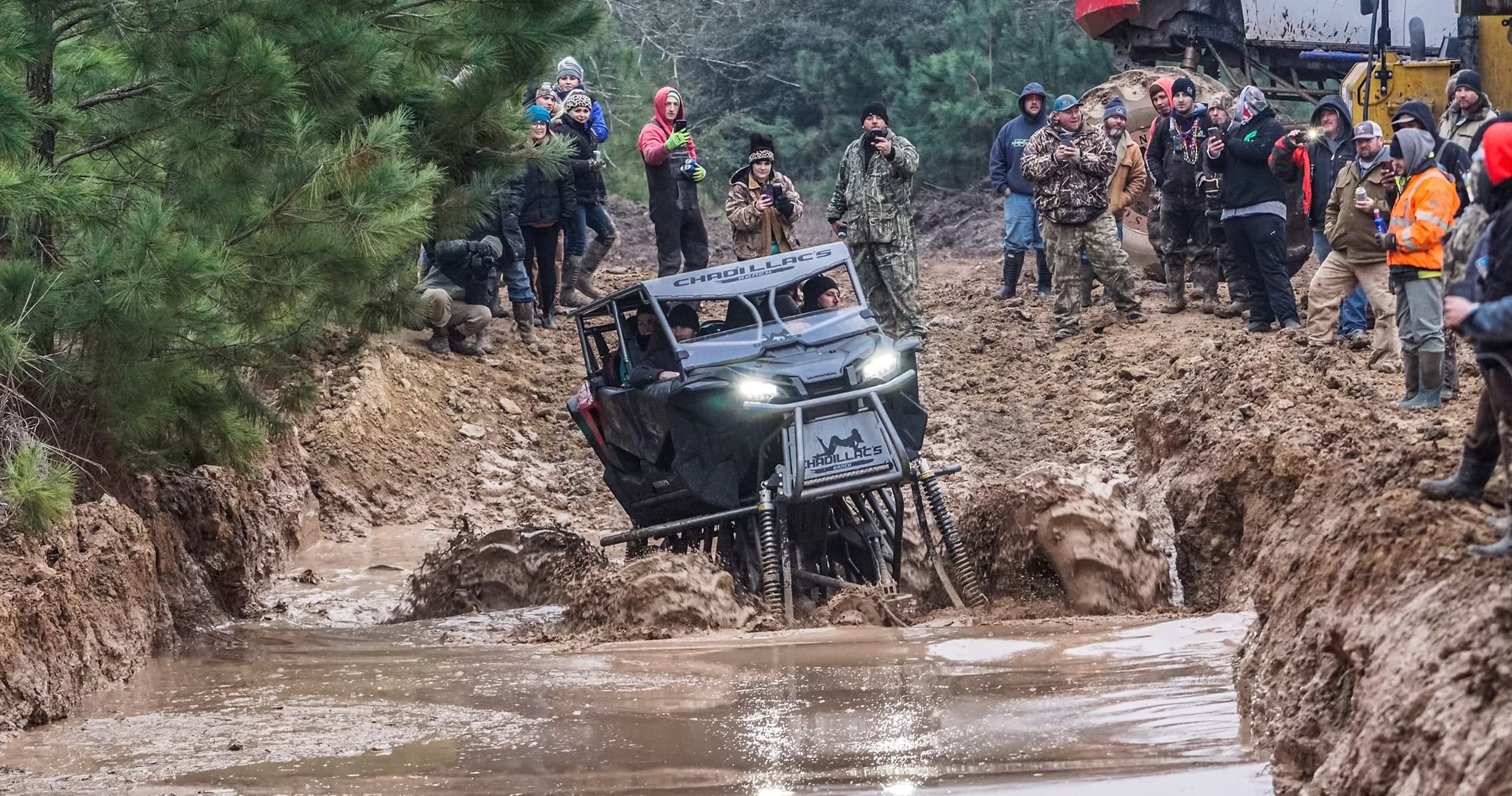 Side-by-side vehicle navigating flooded mud pit with spectator crowd