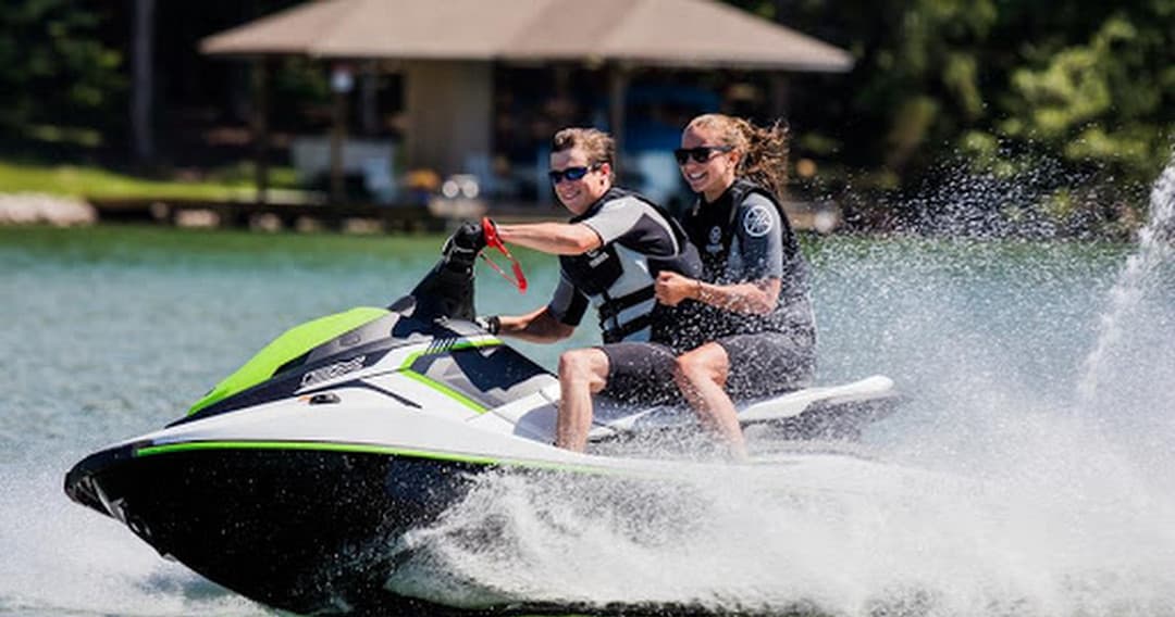 Two riders on a jet ski speeding across a lake near shore