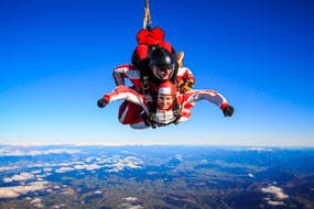 Tandem skydivers freefall over expansive mountain coastline