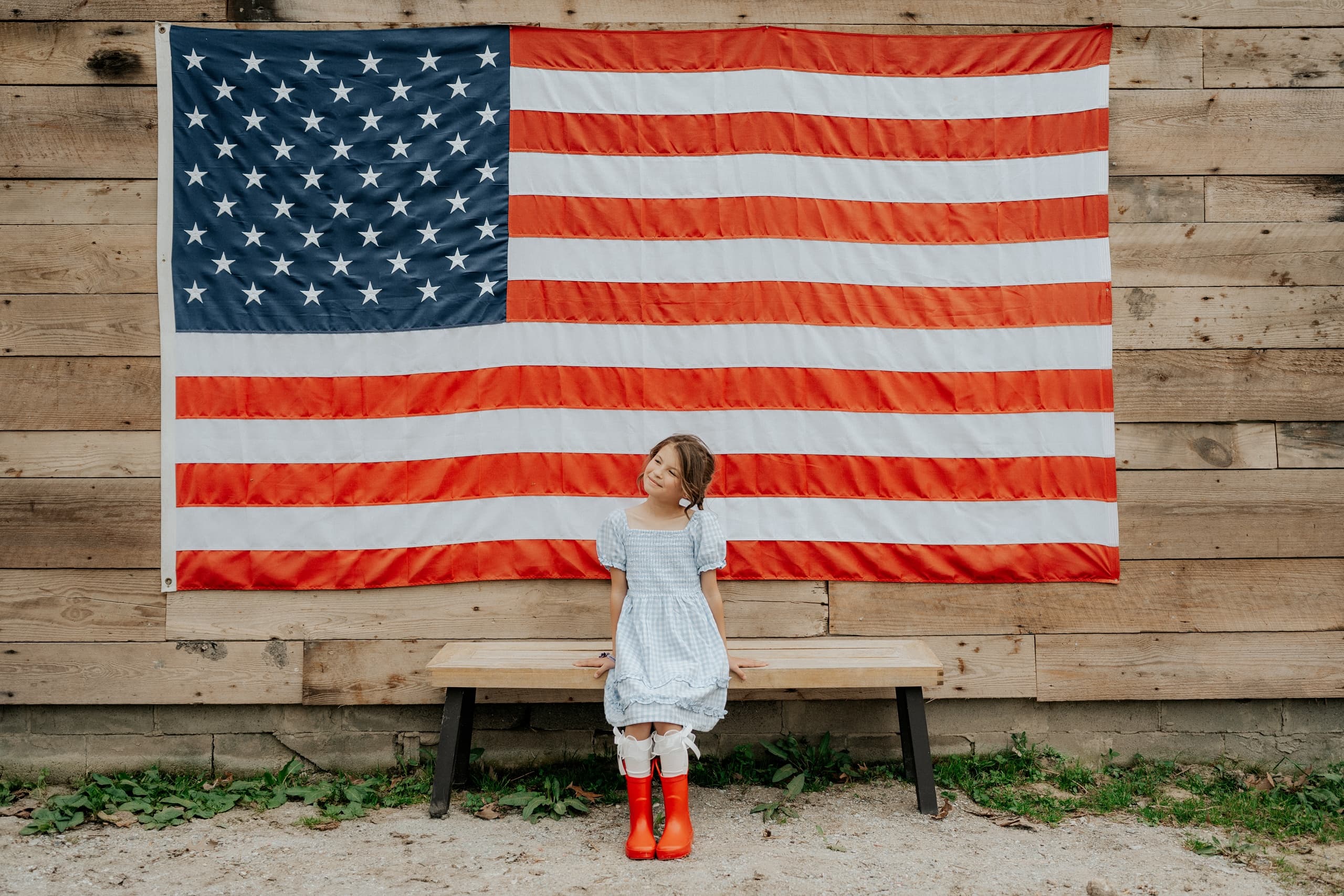 Child standing before American flag on rustic outdoor barn wall