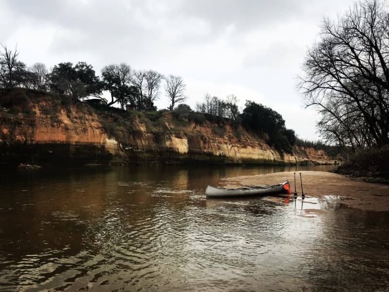 Canoe resting on riverbank under sandstone cliffs at river bend