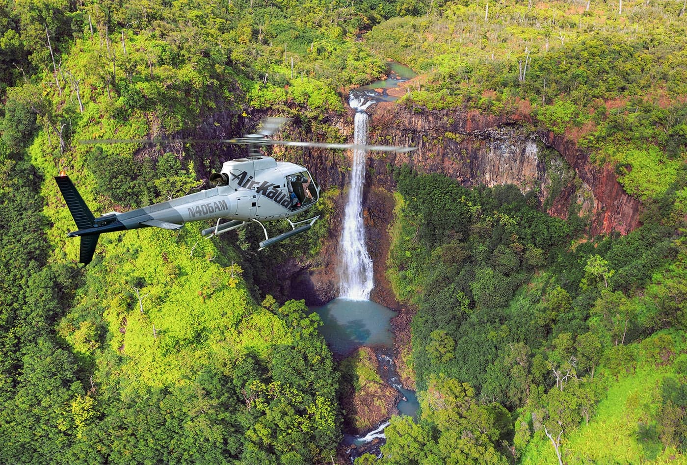 Helicopter near waterfall in Kauai rainforest, scenic air tour