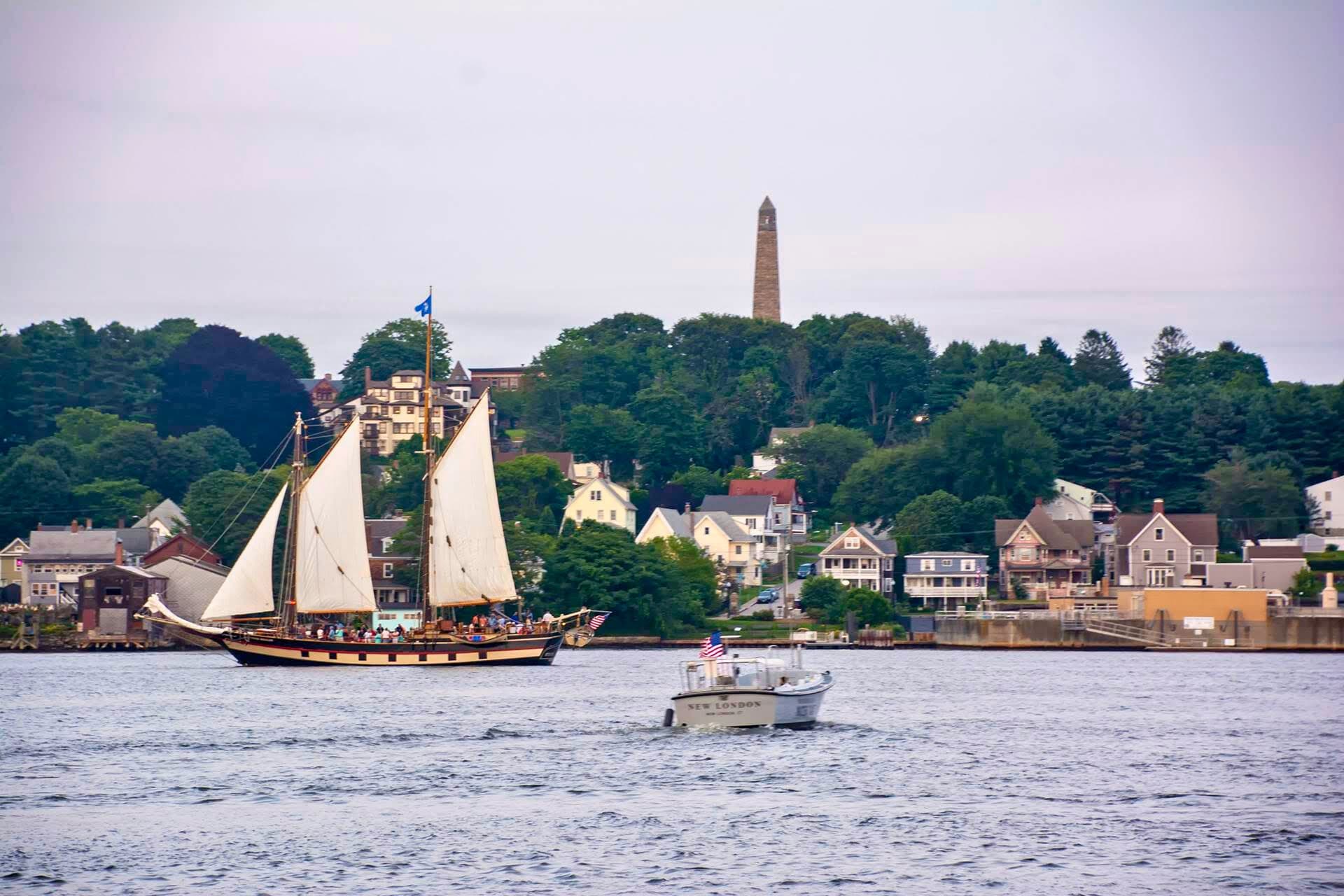 Classic schooner sailing past coastal town near riverside monument