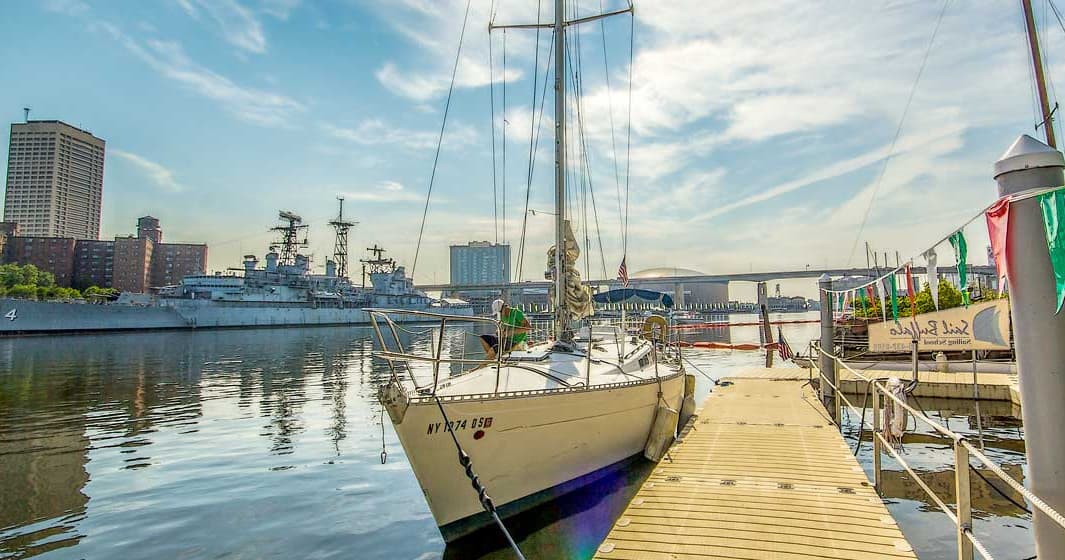 Sailboats moored at a sunny urban marina with bridge backdrop
