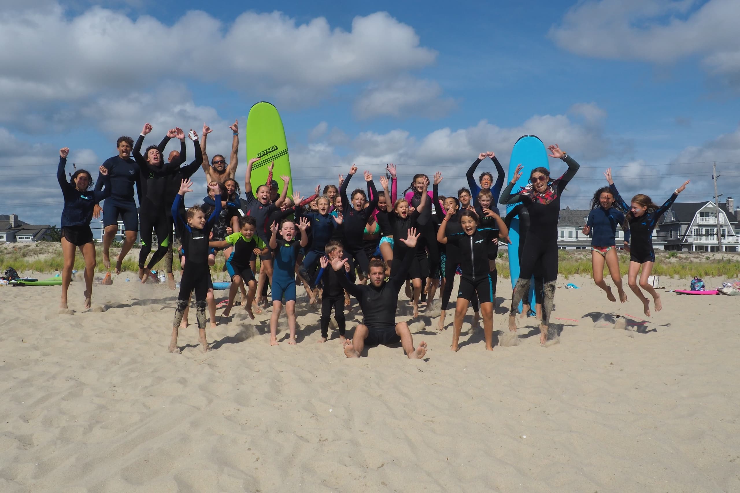 Large surf school group cheering on sandy beach under blue sky